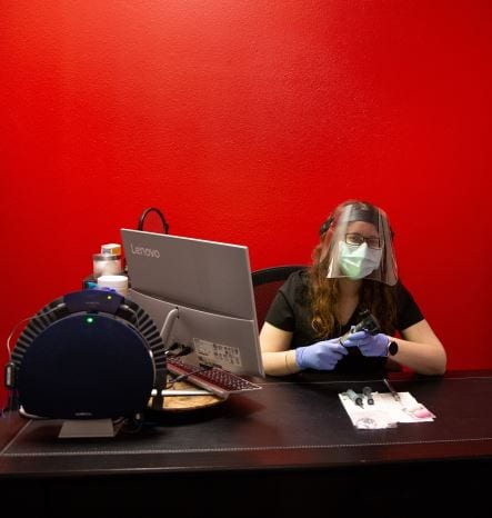 A female audiologist sitting at desk wearing PPE 